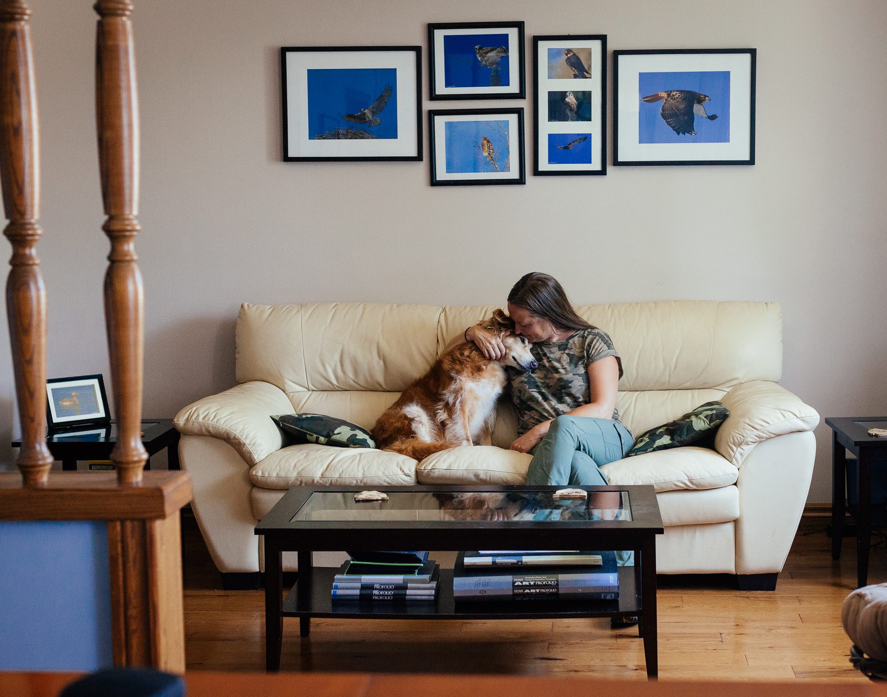 Heidi and her dog, Molly sit under a collection of photographs Heidi and Kelly have taken of different local birds of prey. They've lined the walls in their B&B with photos of all sorts of birds. 